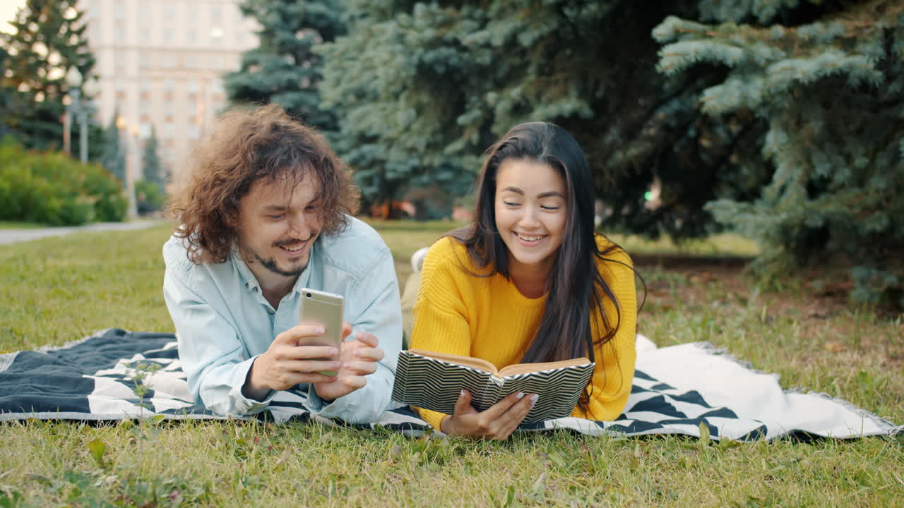 Pareja relajándose en el parque con libro y teléfono