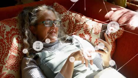 animación de una red de iconos digitales sobre una mujer caucásica usando un teléfono inteligente acostada en el sofá en casa