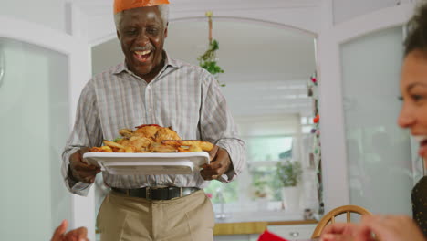 grandfather carrying turkey as multi-generation family sit down to eat christmas meal together