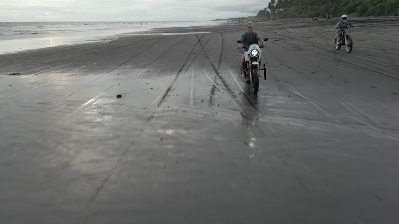 안테나 는 구름진 아침 하늘 과 함께 모래 해변 에 타고 있는 모터사이클 을 이끌고 있다