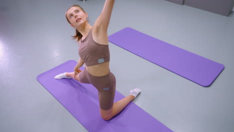 top-down view of person performing deep stretch on purple yoga mat, wearing workout attire, focus on flexibility, balance, and strength during yoga in spacious, well-lit environment