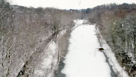 aerial establishing shot of frozen lake, pond during winter snowfall