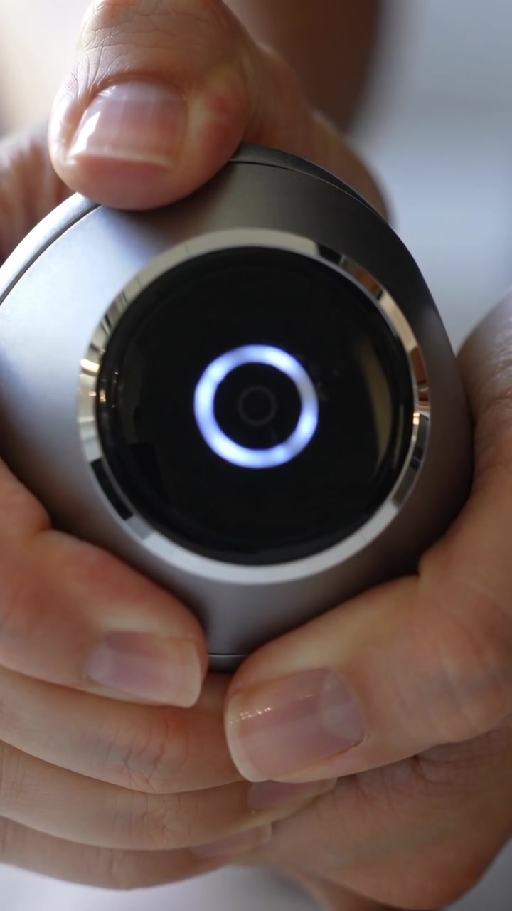 Video verticale: Illuminazione ad anello LED, mani che testano una fotocamera rotonda e regolano la presa in una stanza con luce soffusa.