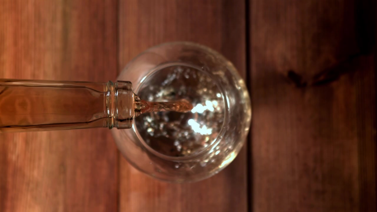 Slowmotion hældning af gylden væske i et glas på et træbord