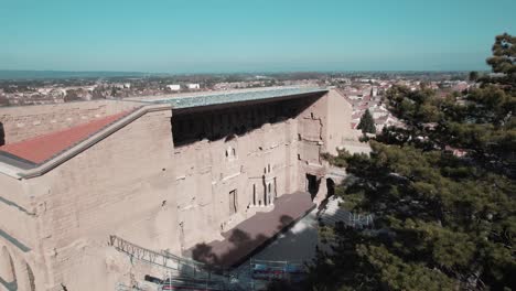 Drone-shot-of-a-huge-fir-tree-ending-on-the-monument-of-an-ancient-theater