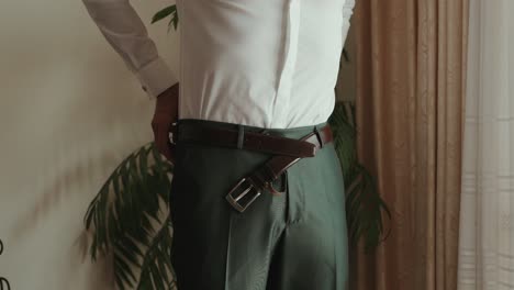 groom tightens belt over dress pants in natural indoor light