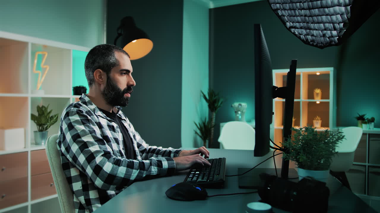 fotógrafo independiente profesional que escribe correos electrónicos para sus clientes, sentado detrás del escritorio trabajando en una computadora de escritorio usando el teclado y el mouse mientras mira el monitor dentro del moderno estudio de oficina en casa