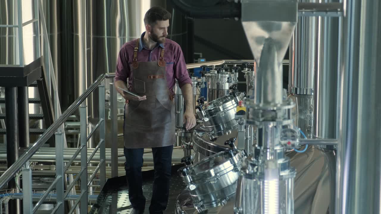 un joven cervecero con un delantal de cuero supervisa el proceso de fermentación de la cerveza en una fábrica de cerveza moderna