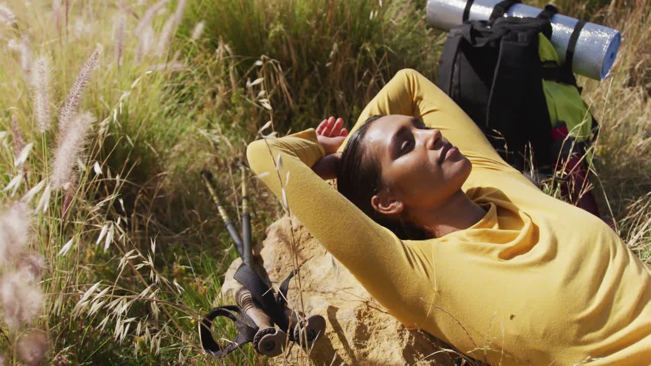 mujer afroamericana acostada en una roca mientras hace senderismo en las montañas