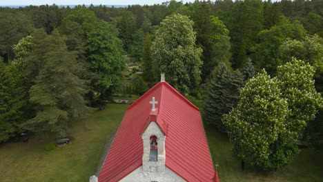 aerial drone revealing shot showing a old country white colored church that has a red roof and bronze bell with a cross on the tower. drone flying backwards and revealing baltic sea in the horizon