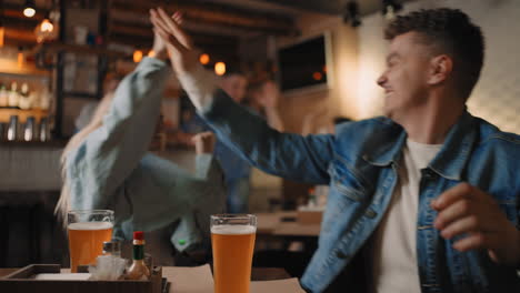 Close-up-of-a-group-of-male-and-female-friends-sitting-together-in-a-bar-and-watching-a-broadcast-on-TV-enjoying-a-goal-scored-shouting-and-hugging.-football.