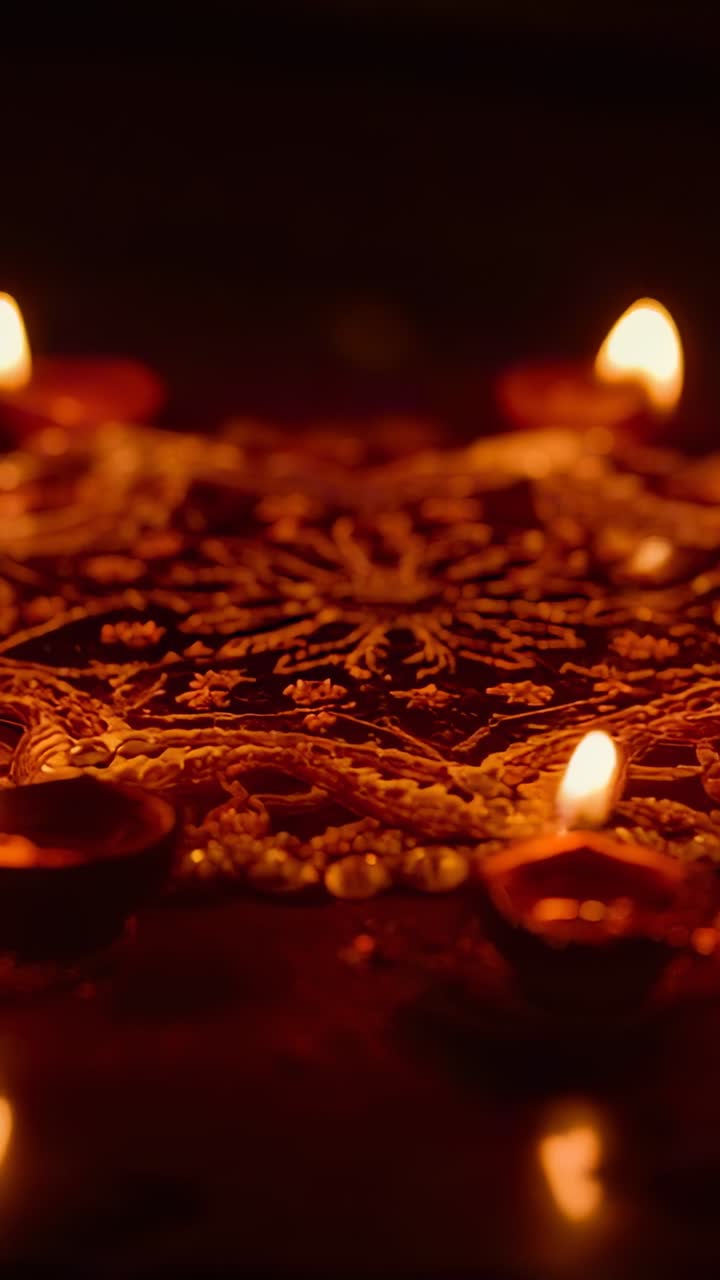 Vertical video: Shifting camera panning over ornate rangoli in home entry, revealing four lit diyas