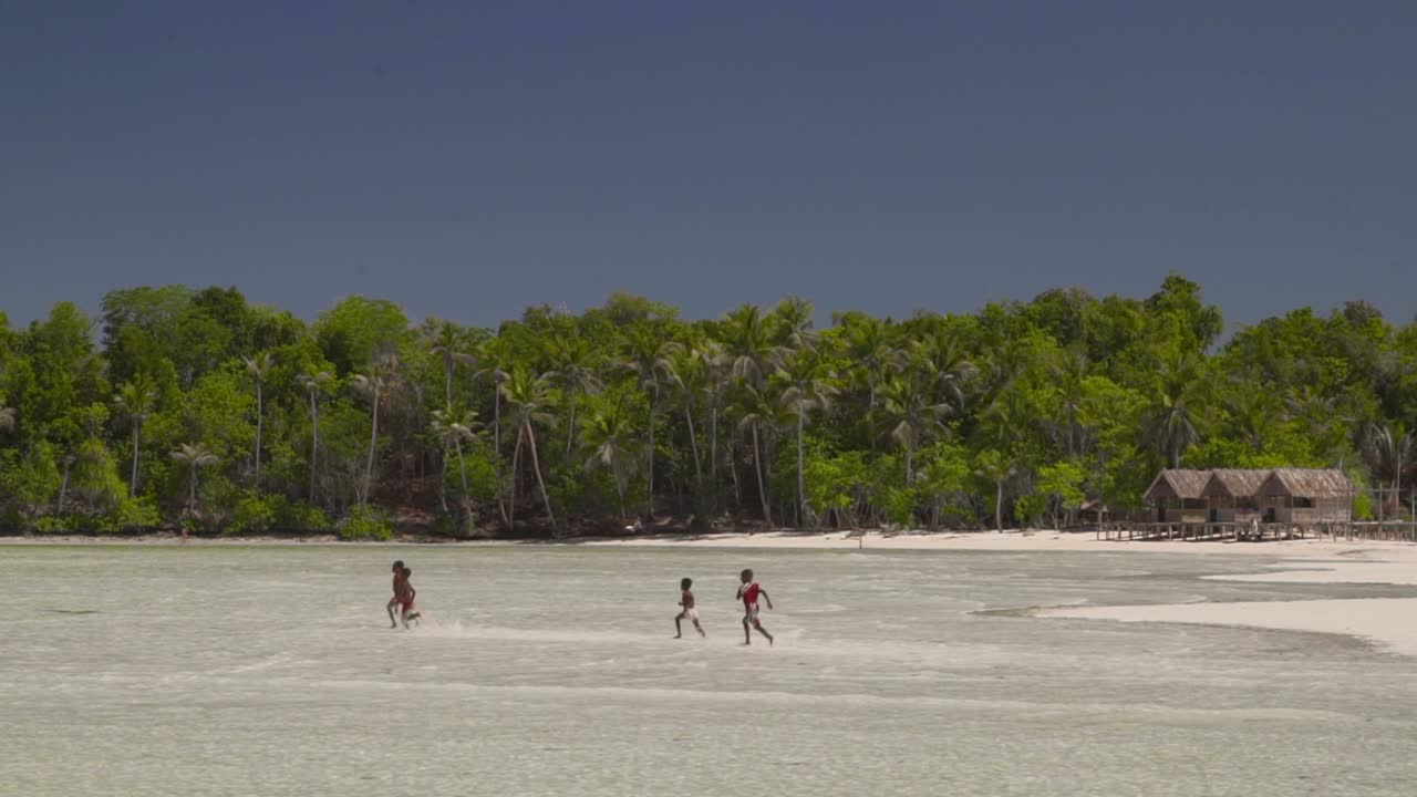 four asian children is running on a white sandy paradise beach. despite not having a lot still very happy