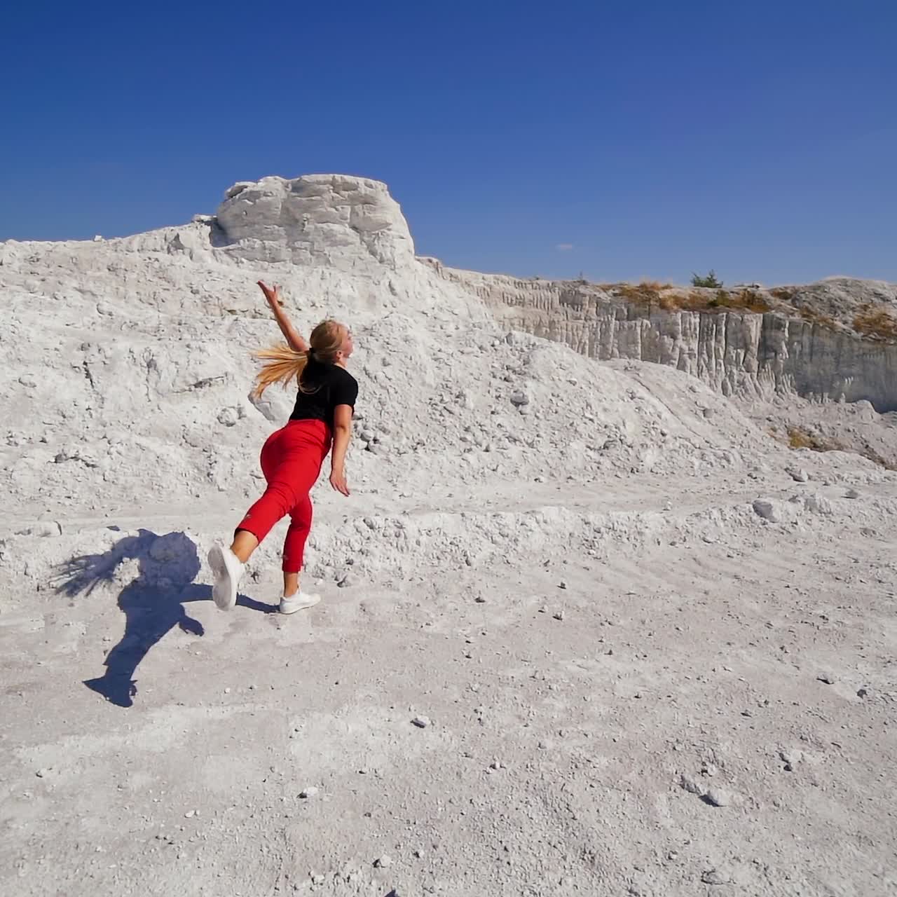 Young girl showing dance move in the rocky locality on sunny day. Dancer jumps and turns at the backdrop of blue sky