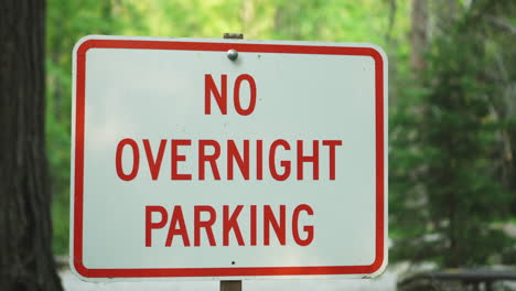 No overnight parking sign in Glacier NP Campground and Creek with green trees in the background