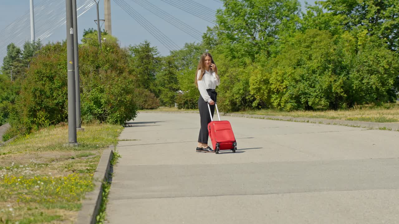 Elegant woman with red suitcase, talking on phone and waving at camera