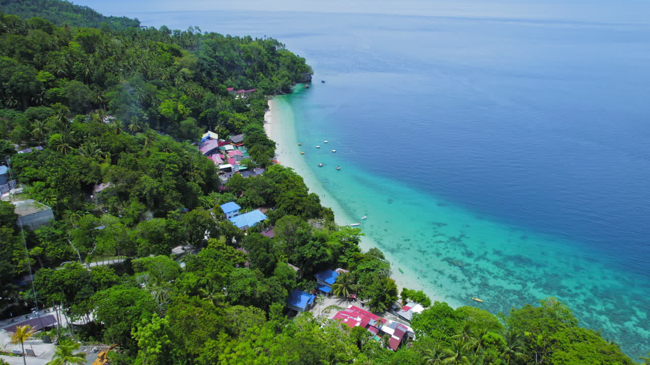 toma cinematográfica de la playa de arena blanca tropical con árboles verdes exuberantes, edificios locales y orilla azul turquesa