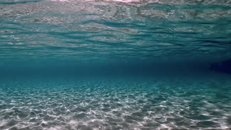 authentic underwater scene of crystalline turquoise tropical sea water with rippled surface and reflections on seabed with blue background