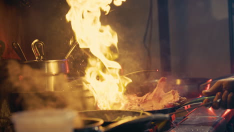 meat sizzles in a flaming pan in a commerical kitchen