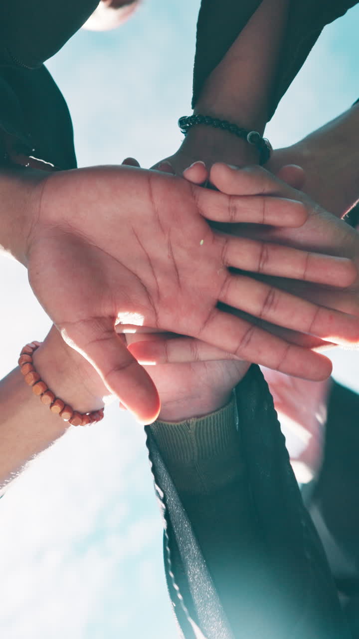 Vista em ângulo baixo de mãos diversas se juntando para trabalho em equipe.
