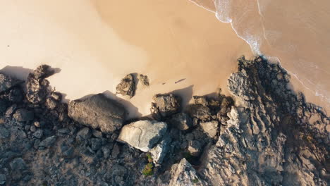 ascending top down shot of person at rocky coastline and ocean in portugal - sandy beach during sunny day