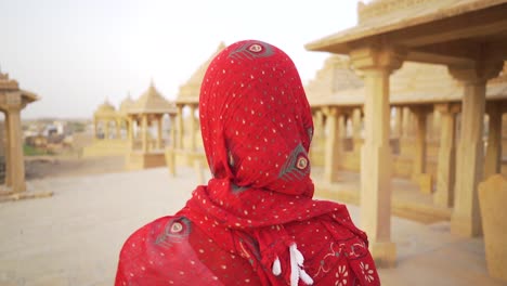 a woman in a saree moves slowly and mysteriously through the sandstone cenotaphs of bada bagh, jaisalmer, india, creating an atmospheric and cinematic scene.