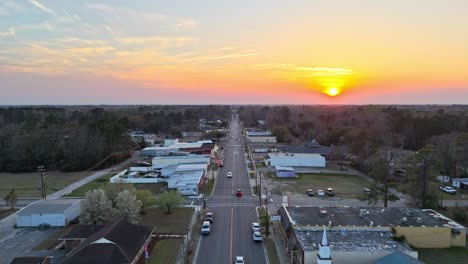 an aerial view of the main street in downtown johnsonville, sc lined with businesses, churches, and homes. an orange and yellow sunset lights up the sky in the distance.