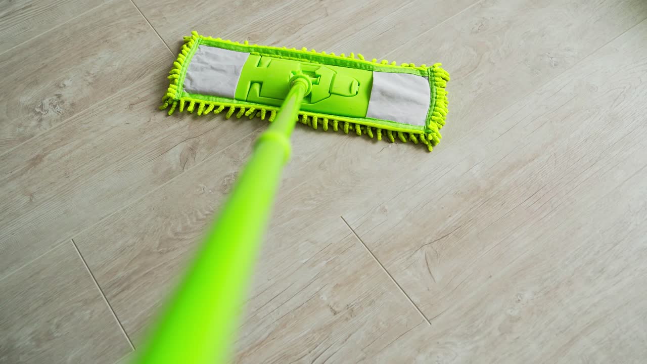 New green mop moving on parquet floor. Cleaning the house with a microfiber mop. Domestic chores. Close-up.