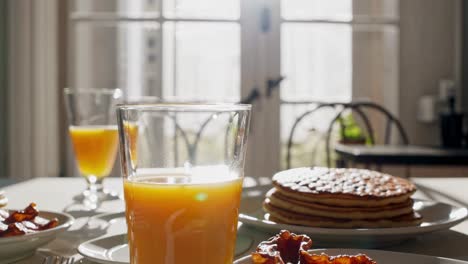 bright kitchen interior featuring sunlight illuminated breakfast table with golden brown pancakes, crispy bacon, fresh orange juice, and steaming coffee mug