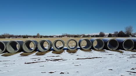 Bewegende-Drohnenaufnahme-Von-Betonrohren-Im-Schneebedeckten-Weizenfeld