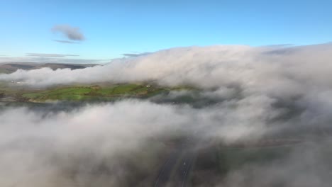 volando por encima de una nube baja hacia una ladera envuelta en niebla con tráfico visible por debajo en la autopista m6