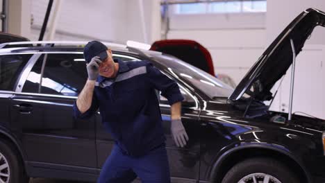 Happy-mechanic-man-in-uniform-and-gloves-dancing-funny-in-a-modern-service-auto-center