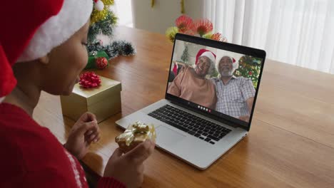 Mujer-Afroamericana-Con-Sombrero-De-Santa-Usando-Una-Computadora-Portátil-Para-Una-Videollamada-Navideña-Con-Una-Pareja-En-La-Pantalla