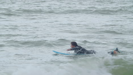 Hombre-Deportivo-En-Traje-De-Neopreno-Con-Pierna-Artificial-Acostado-En-La-Tabla-De-Surf-Y-Nadando-En-El-Océano-2