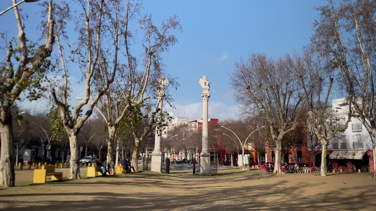 Piazza Alameda de Hercules in una giornata di sole, con colonne antiche, percorsi pedonali e persone che si rilassano all'aperto.