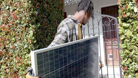 african american man holding photovoltaic panel entering property, slow motion