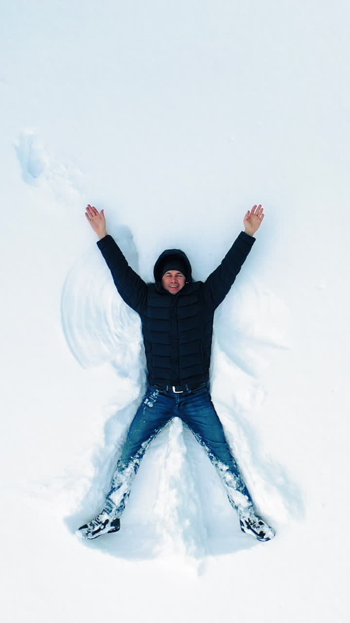 Man lying on snow in winter holiday. Aerial view of snow angel made by man in the snow. Vertical video