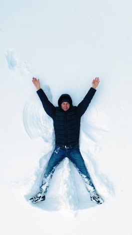 man lying on snow in winter holiday. aerial view of snow angel made by man in the snow. vertical video