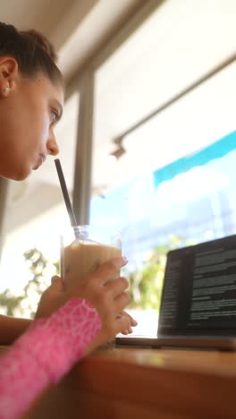 mujer trabajando en una computadora portátil en una cafetería bebiendo café helado