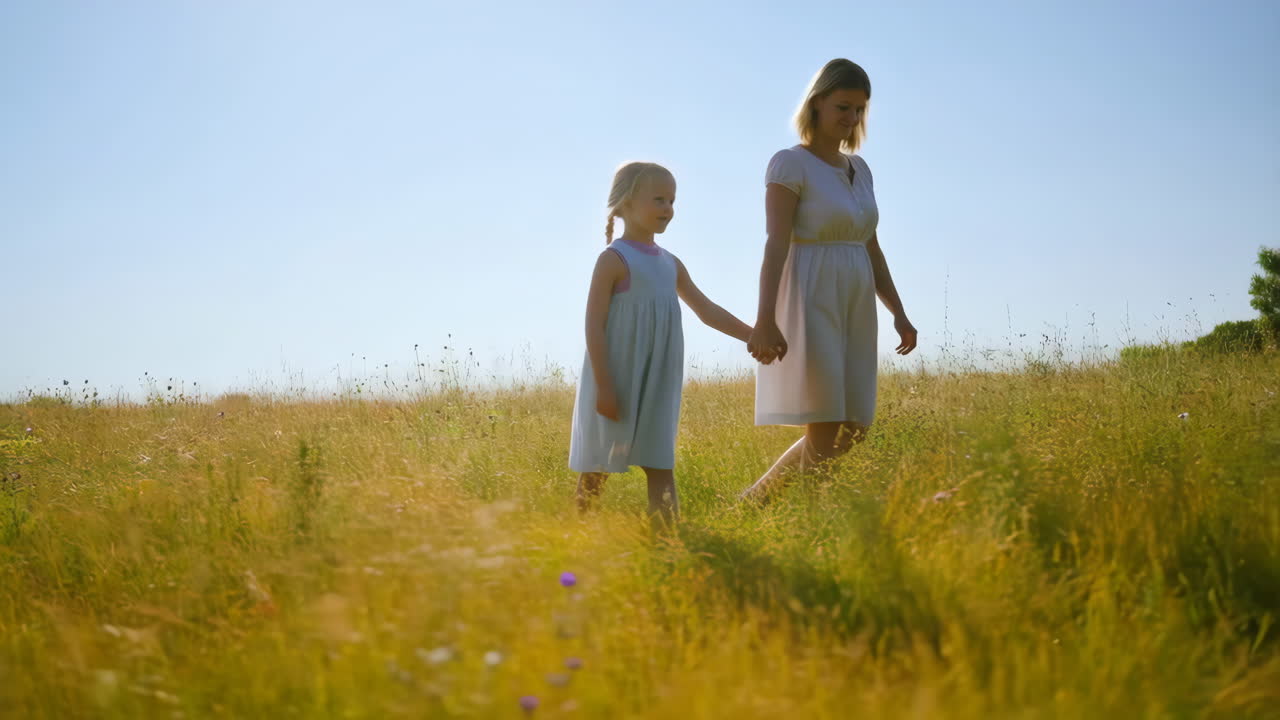 Madre e figlia che camminano mano nella mano attraverso un campo soleggiato