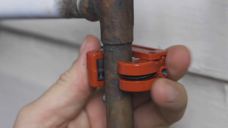 male hands turn an orange pipe cutter to open an old copper pipe