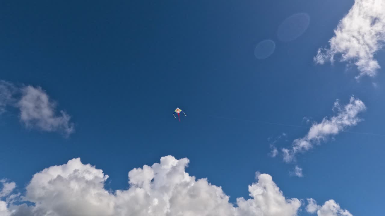 Bambini corrono in un parco, tenendo in mano le corde degli aquiloni. Gli aquiloni volano alti nel cielo mentre le nuvole passano. Le famiglie si godono il tempo all'aperto in una giornata calda