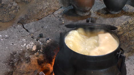 old cauldron being stirred by a spoon over a fire to cook food