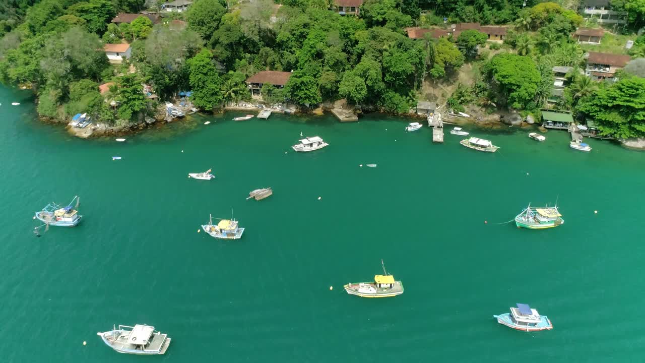 Riprese aeree orbitali con drone di numerose imbarcazioni vicino alla costa di una foresta tropicale con vegetazione densa e poche costruzioni.