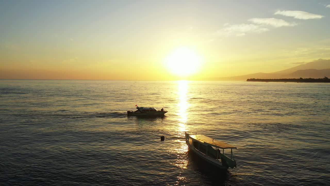 Touring boat sailing toward shore of tropical island at sunset with yellow sky reflecting on calm sea surface in Malaysia
