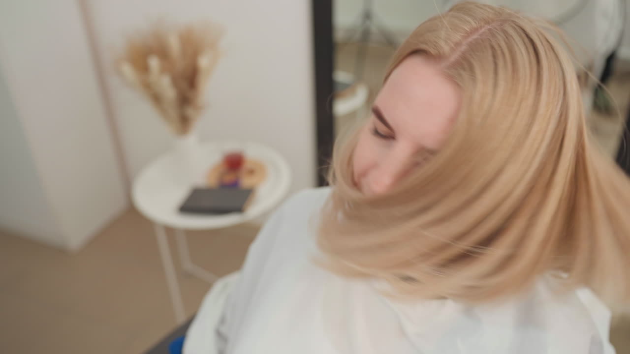 Una mujer caucásica rubia con un corte bob encrespado en un estudio con un espejo y una decoración de flores secas enmarcan un estilo moderno de media melena texturizada mientras sacude la cabeza, mostrando la textura rizada, el volumen y el movimiento editorial.