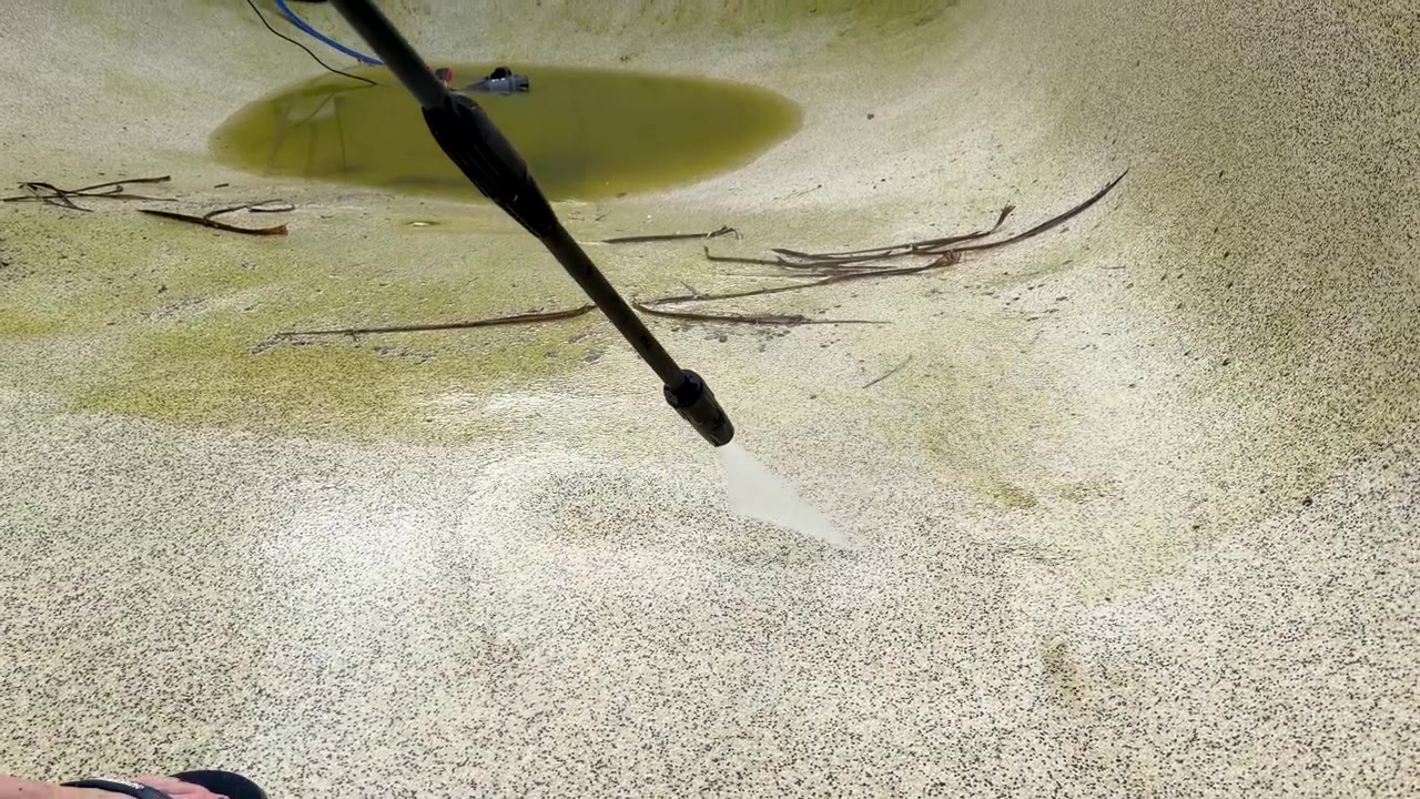 En højtryksrenser fjerner grønne alger og snavs fra en betonpooloverflade i slow-motion.