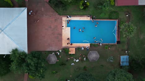 top-down drone shot over the property with pool with people enjoying and parting