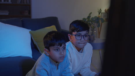 Dos-Niños-Pequeños-En-Casa-Jugando-Con-Una-Consola-De-Juegos-De-Computadora-En-La-Televisión-Sosteniendo-Controladores-A-Altas-Horas-De-La-Noche