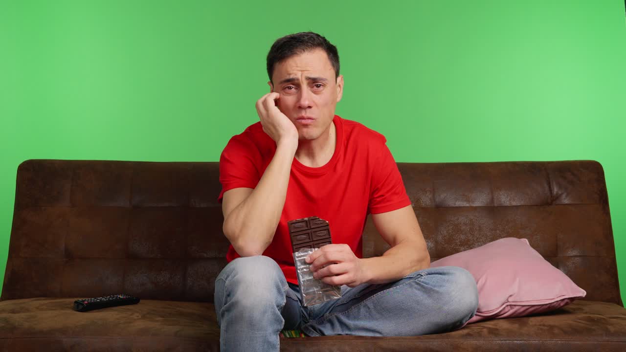 Sad man eating chocolate watching movie on green screen